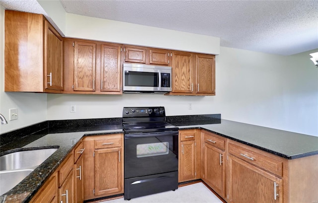 kitchen featuring stainless steel microwave, black range with electric stovetop, a sink, a peninsula, and brown cabinets