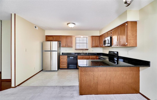 kitchen featuring stainless steel appliances, a sink, a peninsula, brown cabinets, and a textured ceiling