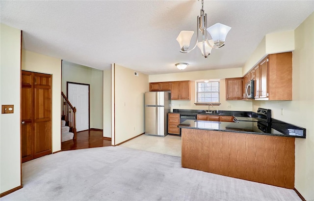 kitchen featuring appliances with stainless steel finishes, a sink, brown cabinets, a peninsula, and dark countertops