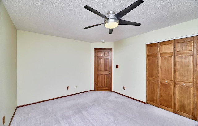 unfurnished bedroom featuring light carpet, baseboards, a ceiling fan, a textured ceiling, and a closet