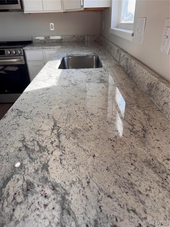 kitchen featuring stainless steel range with electric cooktop, white cabinets, and light stone countertops