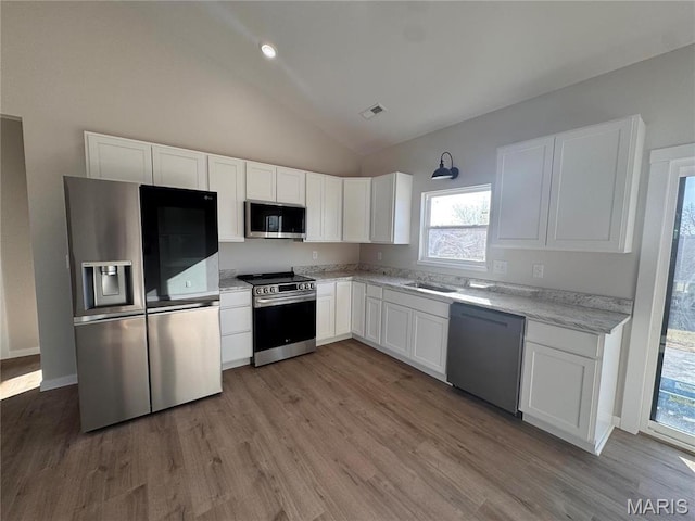 kitchen featuring appliances with stainless steel finishes, vaulted ceiling, white cabinets, wood finished floors, and a sink