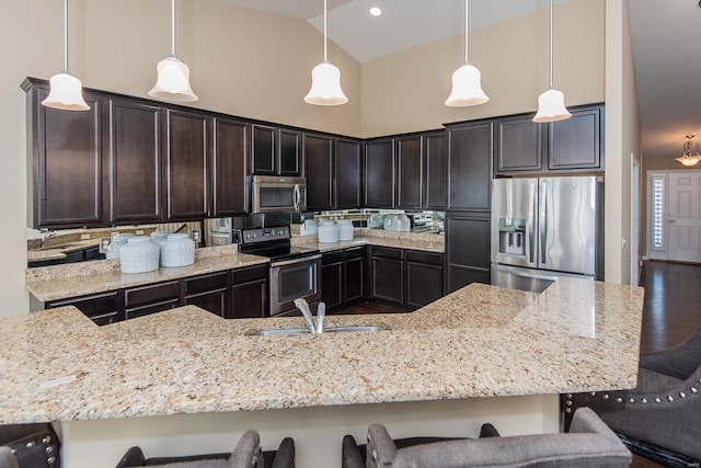 kitchen featuring appliances with stainless steel finishes, a sink, light stone countertops, high vaulted ceiling, and a kitchen bar