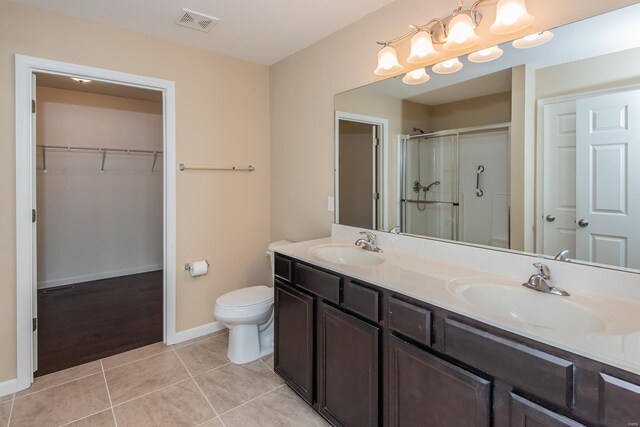 full bathroom featuring a shower stall, baseboards, toilet, double vanity, and a spacious closet