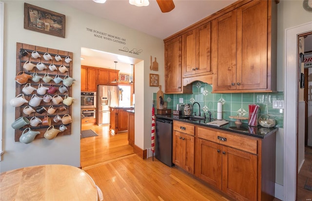 kitchen with stainless steel appliances, light wood-style flooring, dark countertops, a sink, and tasteful backsplash