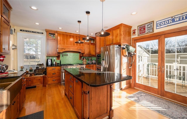 kitchen with stainless steel appliances, backsplash, light wood-style flooring, brown cabinetry, and a center island