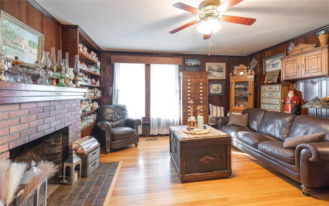 living room featuring wood walls, a ceiling fan, a brick fireplace, and wood finished floors