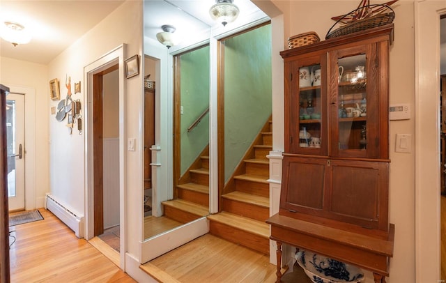 hall with a baseboard radiator, light wood-type flooring, and stairway