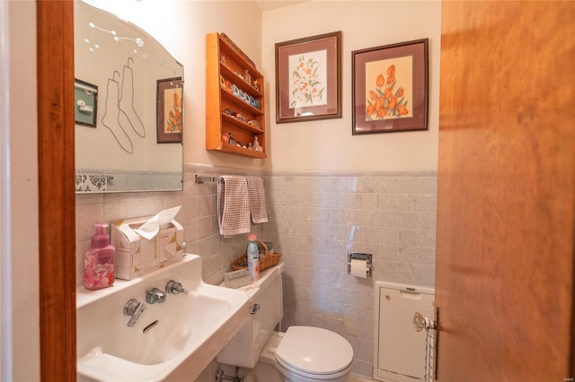 half bath featuring tile walls, toilet, a sink, and a wainscoted wall