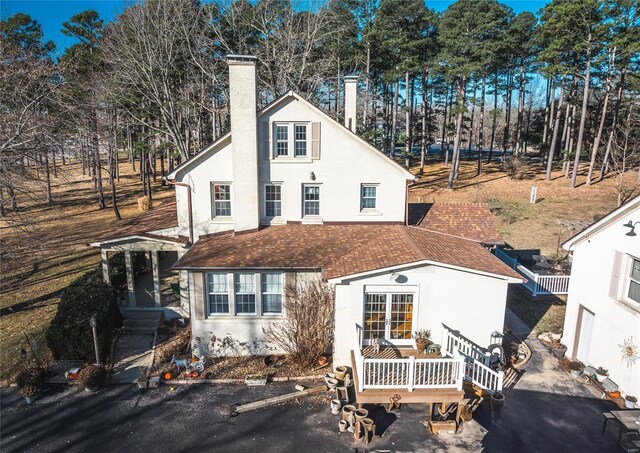 traditional-style home featuring stucco siding, a chimney, and view of wooded area