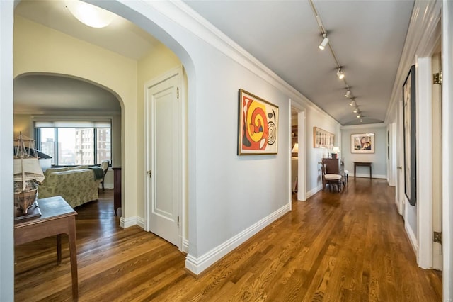 hallway with track lighting, arched walkways, wood finished floors, and baseboards