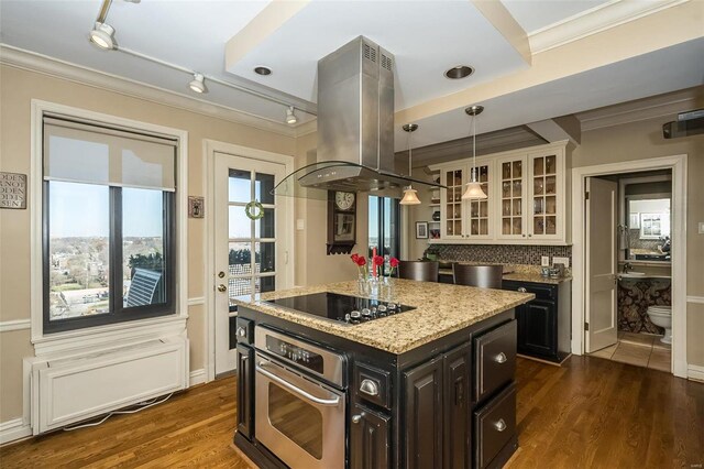 kitchen with oven, island range hood, black electric cooktop, glass insert cabinets, and crown molding