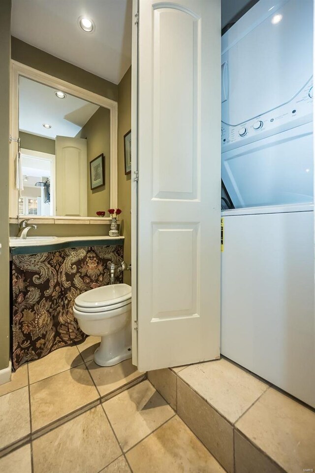 bathroom with estacked washer and dryer, toilet, a sink, and tile patterned flooring