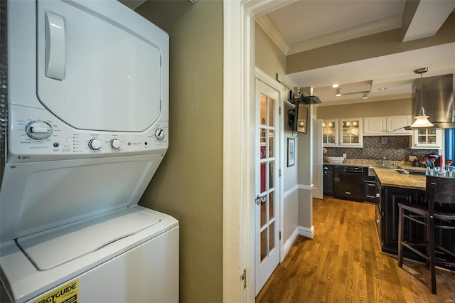 clothes washing area with estacked washer and dryer, wood finished floors, and crown molding