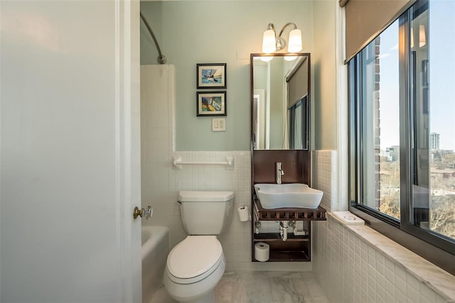 full bathroom featuring healthy amount of natural light, a sink, marble finish flooring, toilet, and tile walls