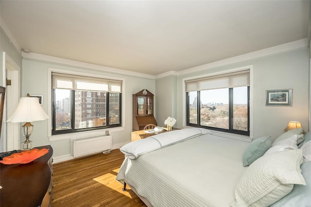 bedroom featuring radiator heating unit, multiple windows, wood finished floors, ornamental molding, and baseboards