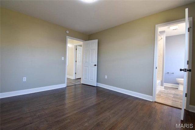 305 E Hauser St, Litchfield, IL 62056 - unfurnished bedroom featuring dark wood-style flooring, baseboards, and connected bathroom