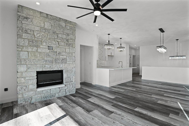 unfurnished living room featuring a ceiling fan, a fireplace, baseboards, a sink, and dark wood-type flooring
