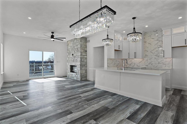 unfurnished living room featuring ceiling fan, a chandelier, a sink, a stone fireplace, and dark wood-style flooring