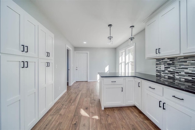 kitchen featuring a peninsula, decorative backsplash, dark countertops, light wood-style floors, and white cabinetry
