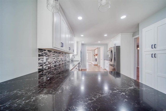 kitchen featuring freestanding refrigerator, tasteful backsplash, white cabinets, recessed lighting, and dark stone countertops