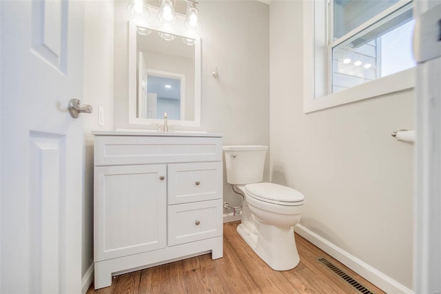 half bath featuring baseboards, toilet, vanity, and wood finished floors