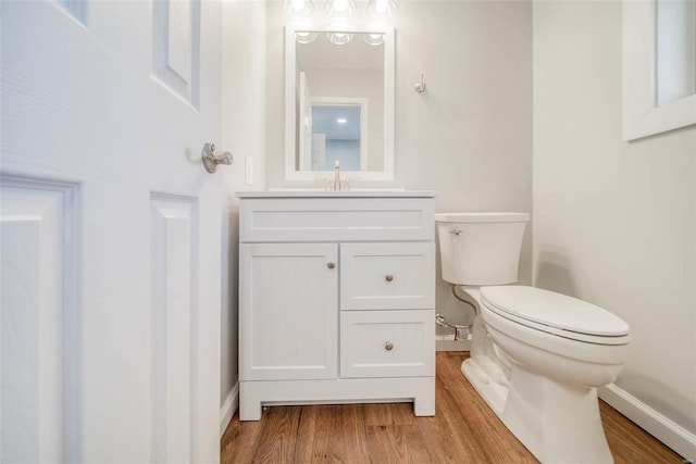 half bathroom featuring wood finished floors, baseboards, toilet, and vanity