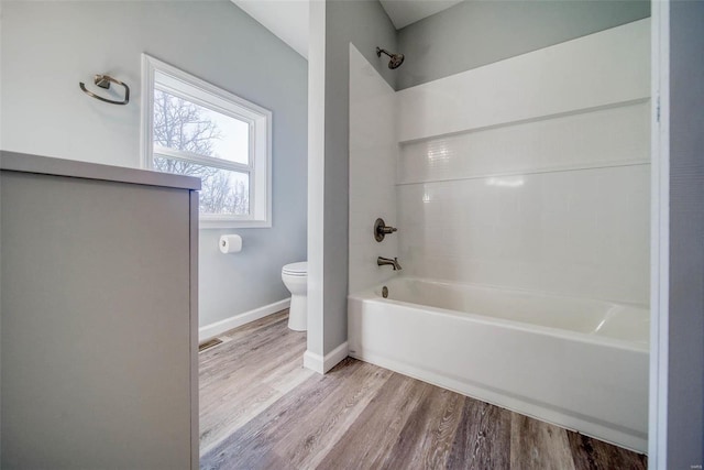 bathroom with toilet, wood finished floors,  shower combination, and baseboards