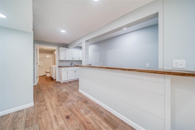kitchen with white cabinets, light wood finished floors, recessed lighting, baseboards, and a sink