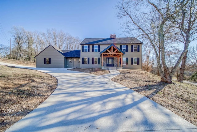 colonial house featuring a chimney, driveway, and a shingled roof