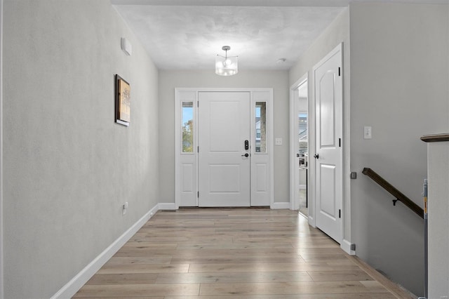 entrance foyer with light wood-style flooring, a chandelier, and baseboards