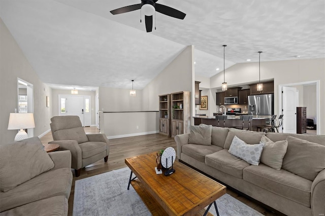 living area featuring wood finished floors, vaulted ceiling, baseboards, and ceiling fan