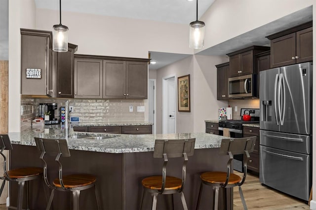 kitchen with appliances with stainless steel finishes, a sink, dark brown cabinets, a peninsula, and tasteful backsplash