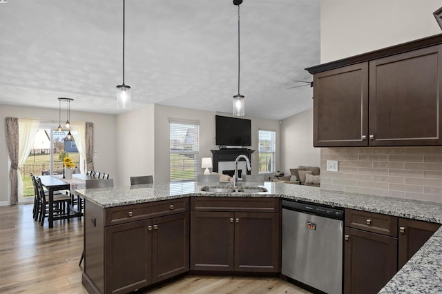 kitchen with stainless steel dishwasher, a sink, dark brown cabinetry, tasteful backsplash, and light wood-type flooring