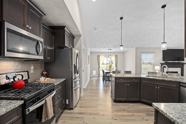 kitchen with stainless steel appliances, a sink, light wood finished floors, and backsplash