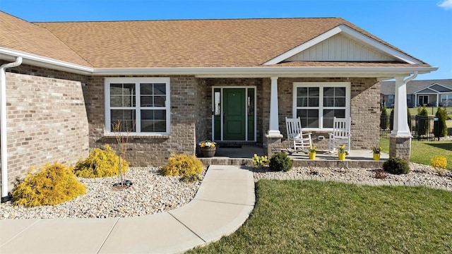 view of exterior entry featuring a porch, brick siding, board and batten siding, roof with shingles, and a lawn