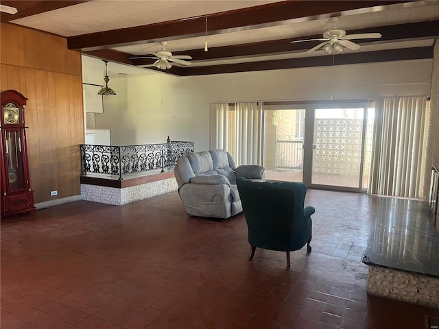 living room with a ceiling fan, beamed ceiling, wood walls, and brick patterned floors