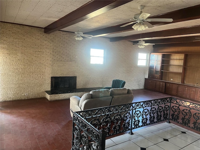 living room featuring brick wall, beam ceiling, a ceiling fan, and a fireplace