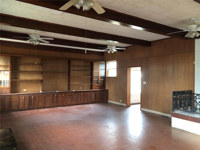 unfurnished living room with a ceiling fan, wooden walls, beamed ceiling, and baseboards