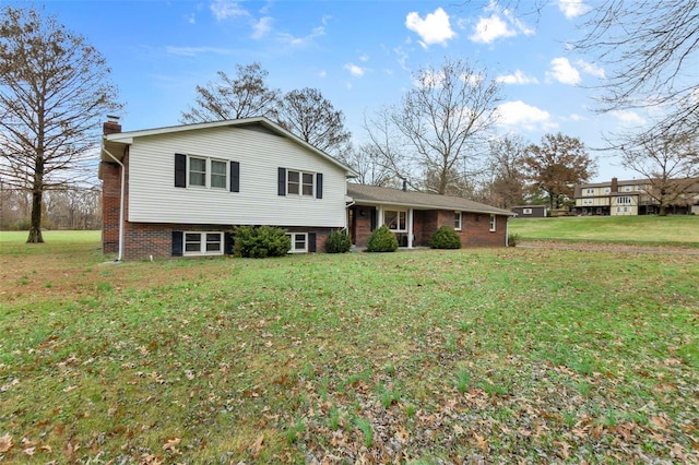 split level home featuring a chimney, a front yard, and brick siding