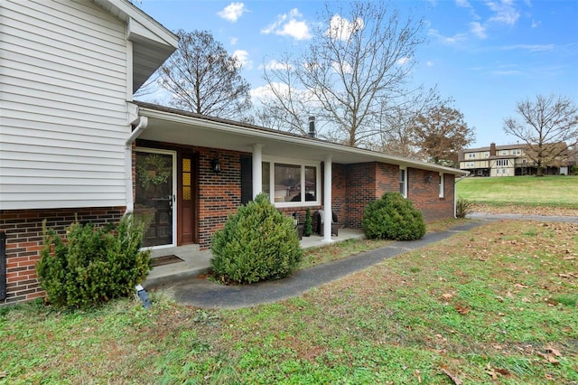 property entrance featuring brick siding, a lawn, and covered porch