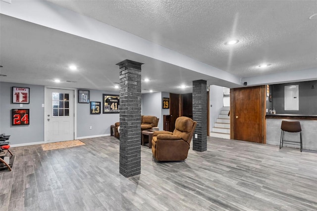 living area with decorative columns, a textured ceiling, baseboards, wood finished floors, and stairs