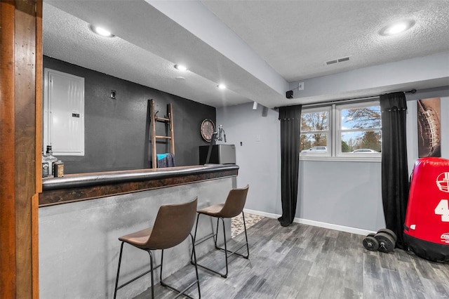 indoor dry bar with electric panel, wood finished floors, a textured ceiling, and baseboards