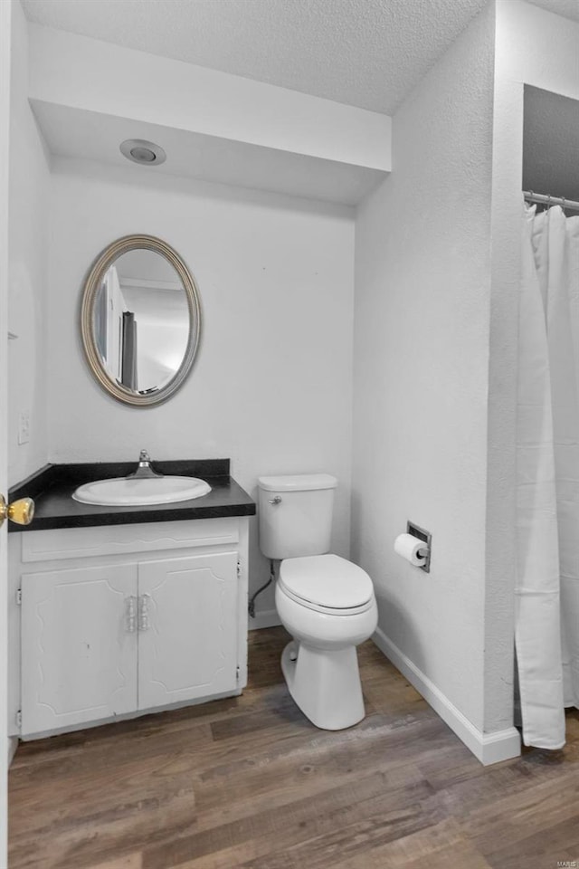 full bathroom featuring wood finished floors, toilet, vanity, a textured ceiling, and baseboards