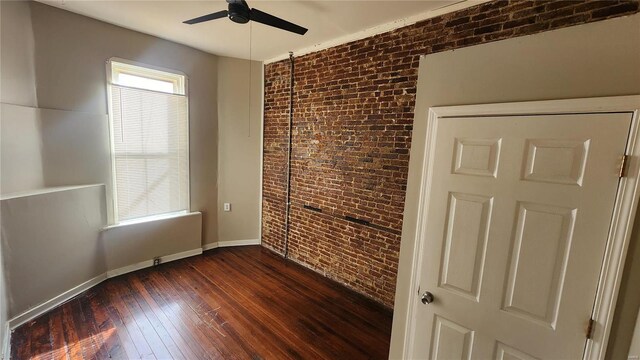 1412 Benton St, Saint Louis, MO 63106 - unfurnished bedroom featuring brick wall, dark wood-style floors, baseboards, a ceiling fan, and an accent wall