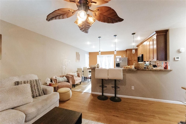 living area featuring light wood-style flooring, ceiling fan, and baseboards