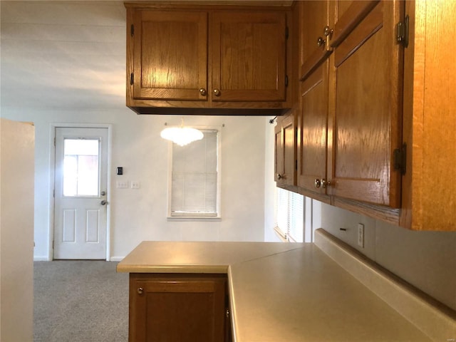 kitchen featuring brown cabinetry, carpet floors, light countertops, baseboards, and a peninsula