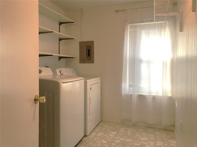 clothes washing area featuring electric panel, washing machine and clothes dryer, light floors, and baseboards