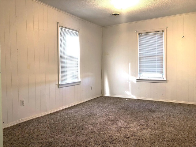 empty room with a textured ceiling, carpet, crown molding, and wooden walls