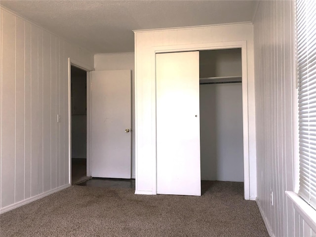 unfurnished bedroom with carpet, a closet, wooden walls, crown molding, and multiple windows
